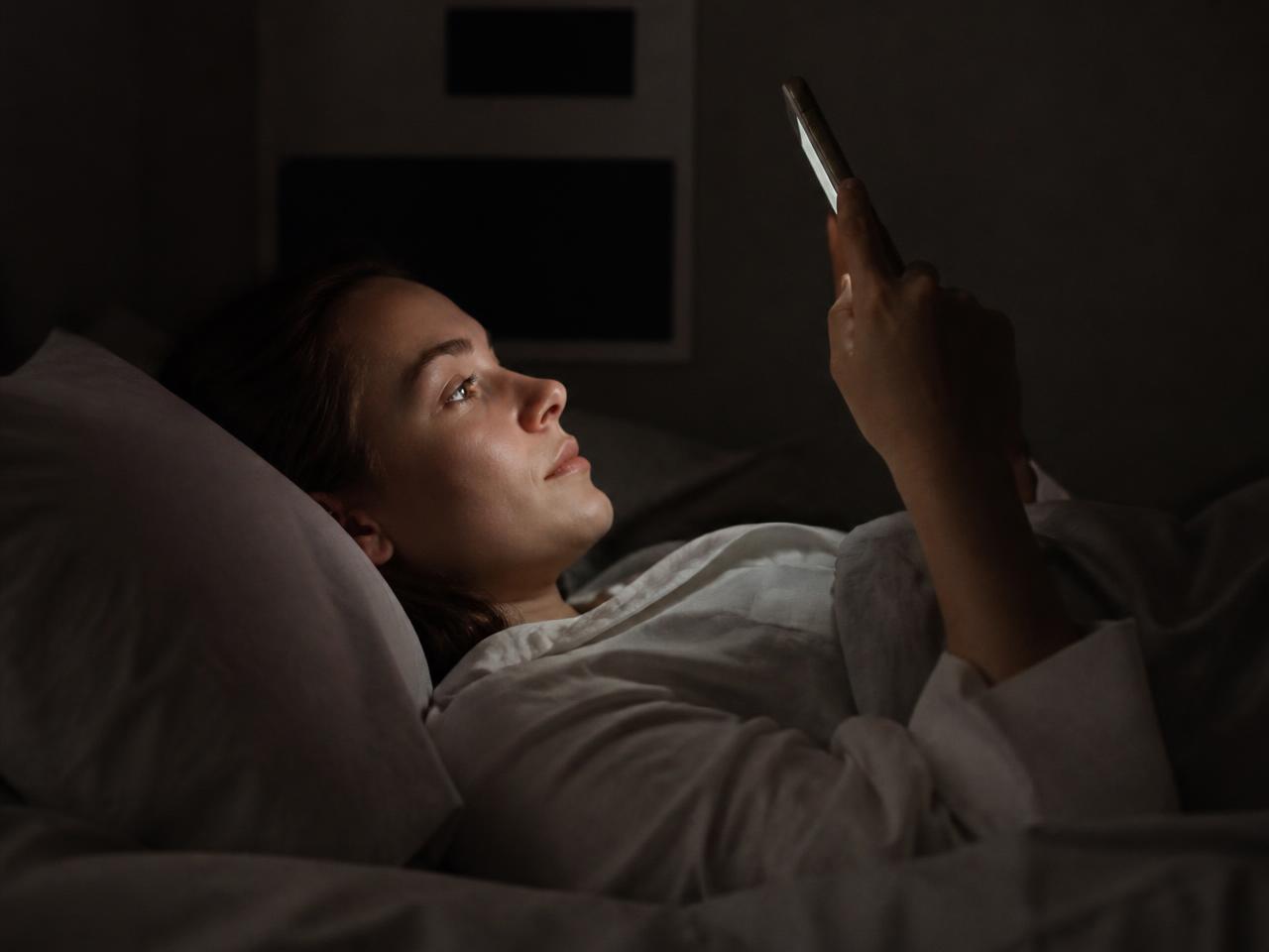 Person in bed at night, face lit by a phone screen