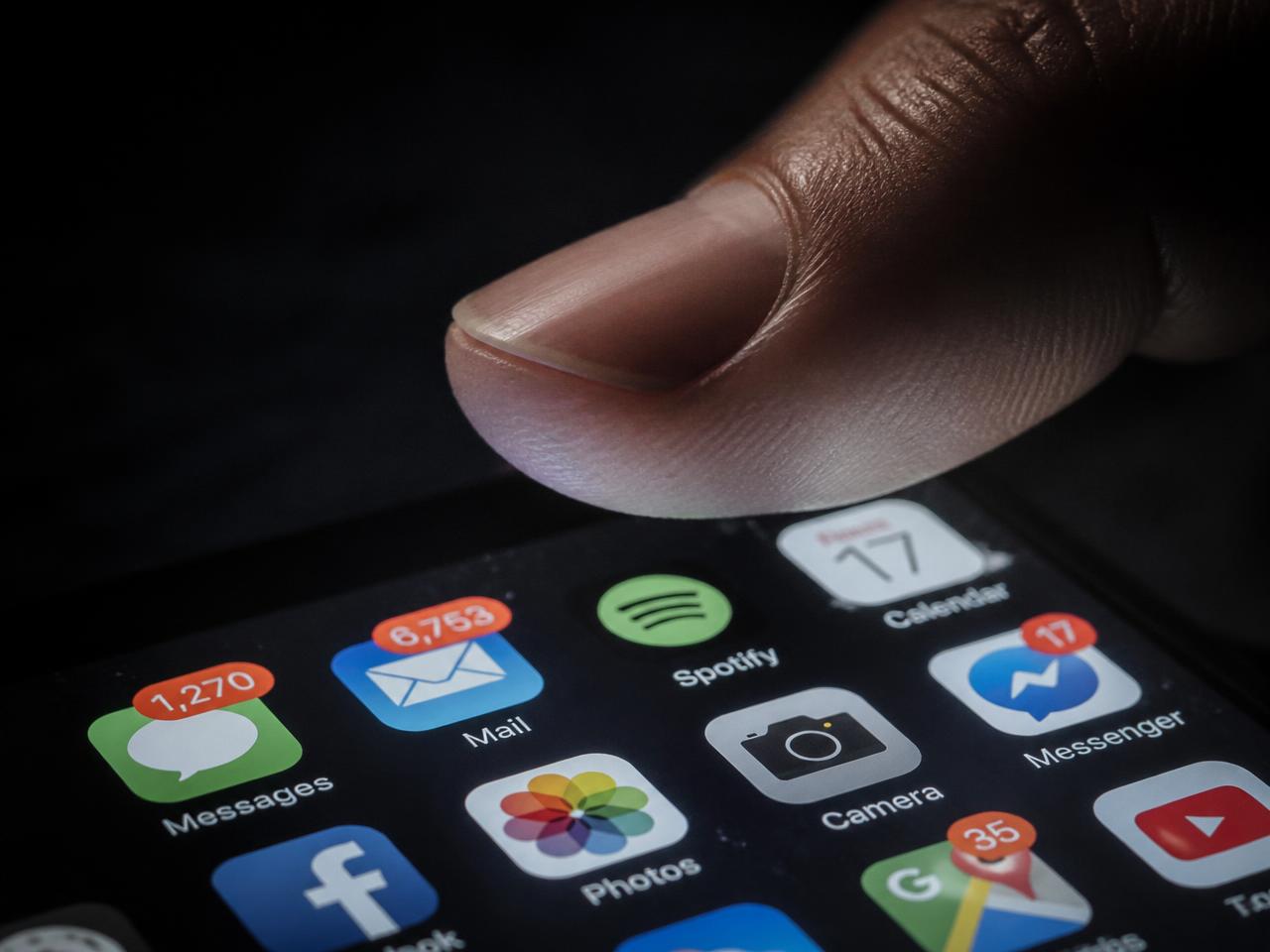 Thumb hovering over a phone screen crowded with notification badges